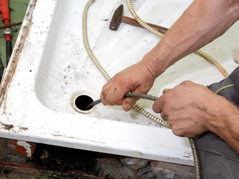 Un plombier utilisant un furet pour déboucher une douche.