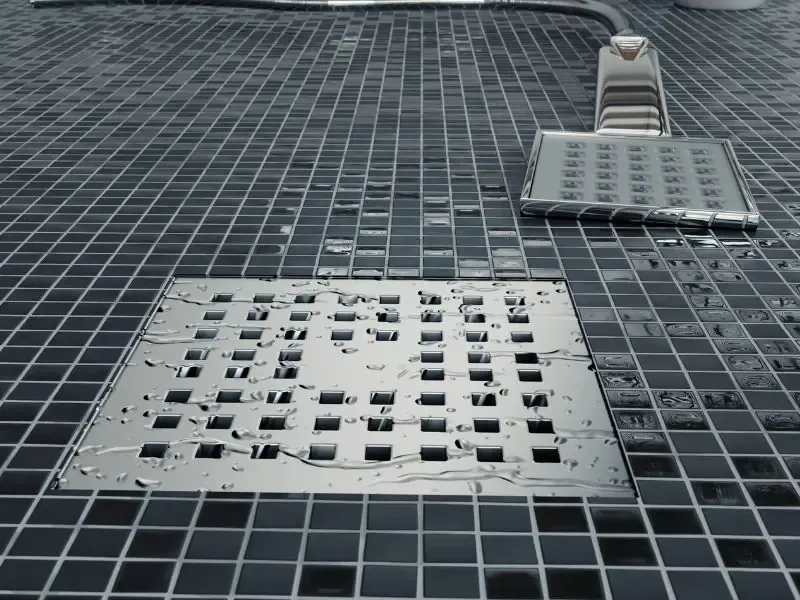 Un drain de douche propre avec des carreaux noirs et une pomme de douche au sol.