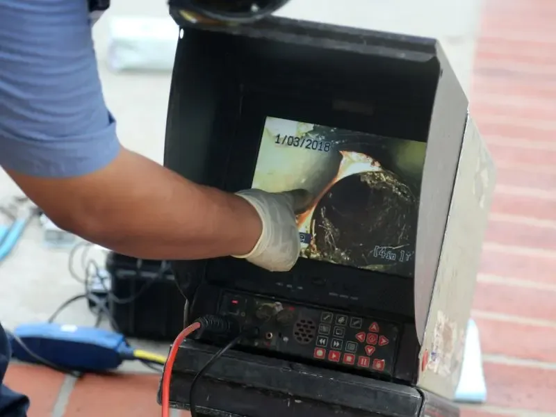Un plombier inspectant l’intérieur d’un tuyau à l’aide d’une caméra d’inspection affichée sur un écran.