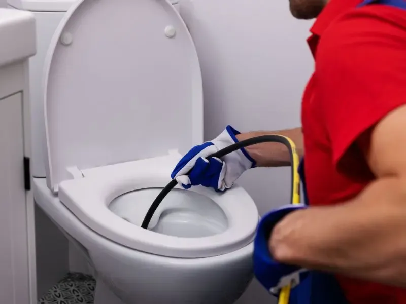 Un plombier utilisant un tuyau haute pression pour déboucher une toilette.