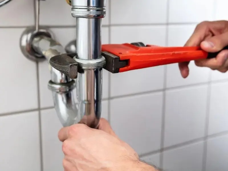 Un plombier serrant un tuyau en métal avec une clé à molette rouge.