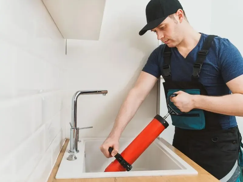 Un plombier utilisant un déboucheur à pression pour déboucher un évier de cuisine.