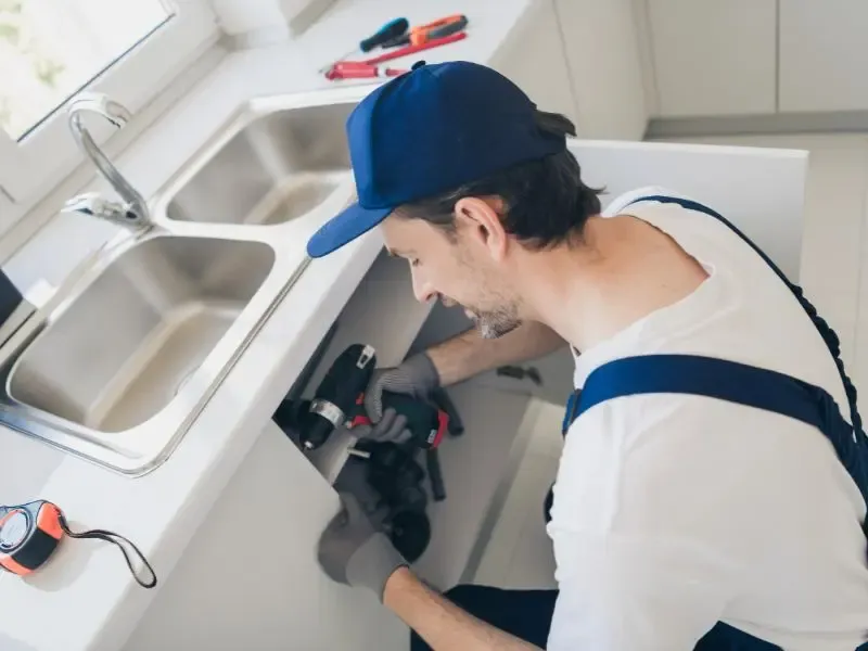 Un plombier inspectant et réparant la tuyauterie sous un évier de cuisine.