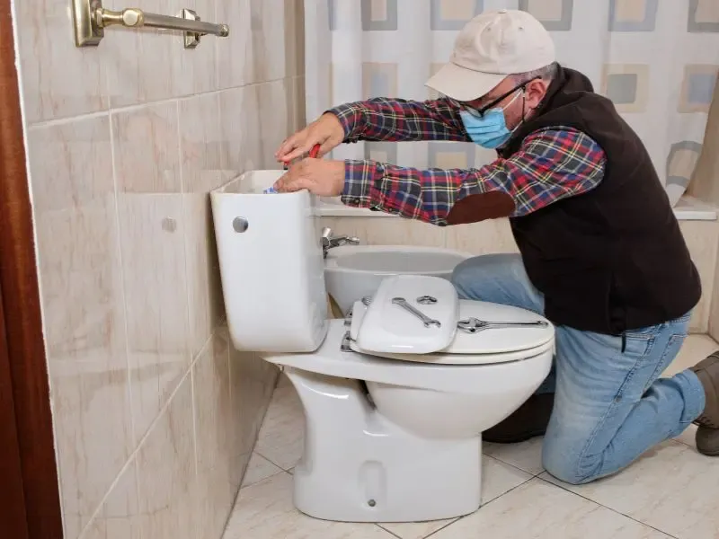 Un plombier en train de réparer la chaîne d’une toilette.
