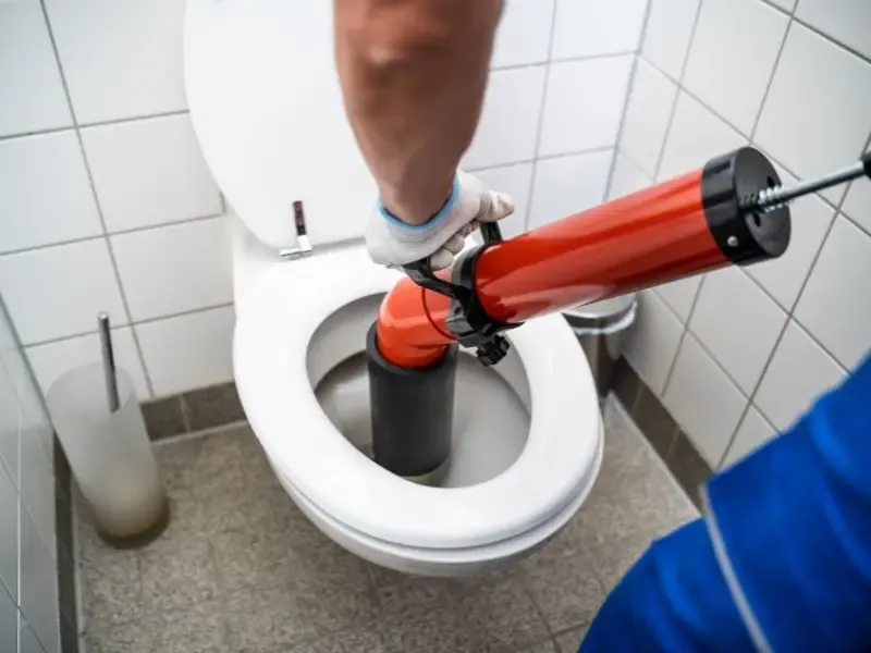 Un plombier utilisant un déboucheur à pression pour déboucher une toilette.